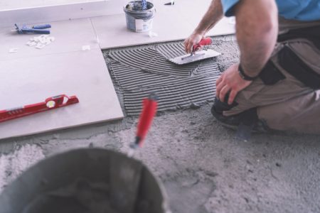 Man applying tile adhesive on the floor Cropped image of adult builder spreading and smoothing tile adhesive on the floor